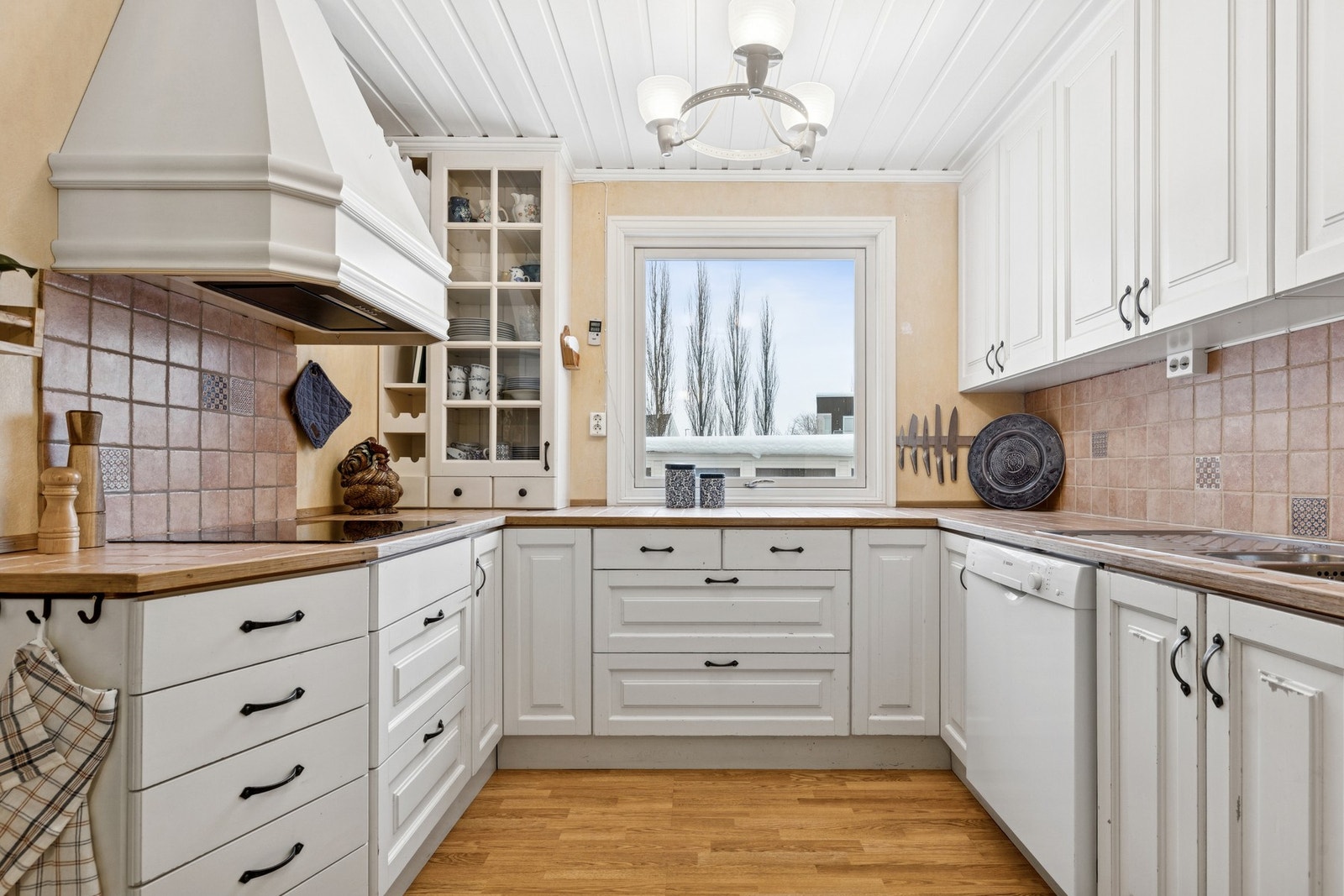 Kjøkkeninnredning med hvitmalte fronter i profilert utførelse, flislagt
benkeplate. Galleribilde