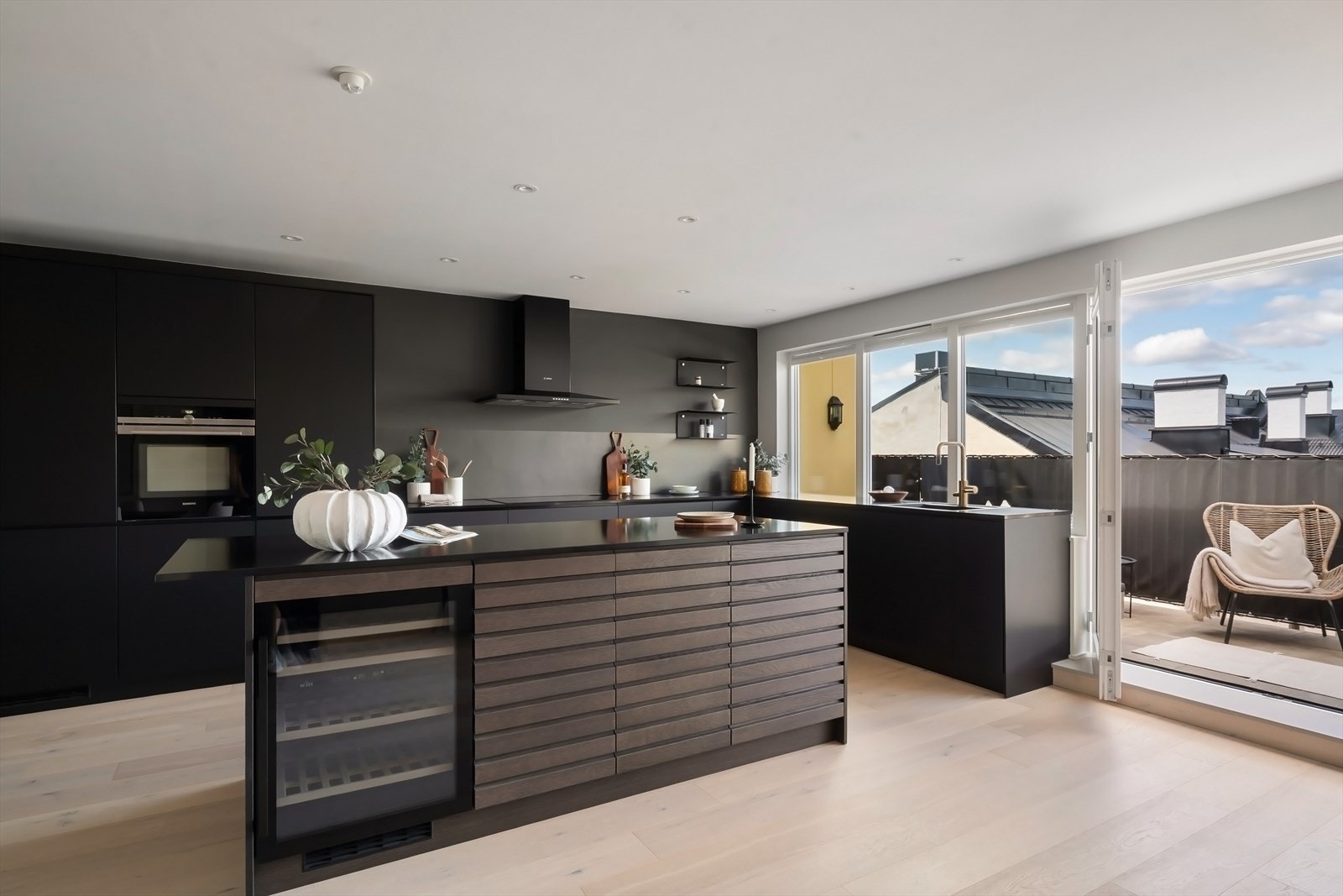 Stilren kjøkkeninnredning fra KVIK med svært praktisk kjøkkenøy. Moderne hvitevarer av god kvalitet: induksjonsplatetopp, stekeovn, kjøleskap, fryseskap i full størrelse, oppvaskmaskin og vinskap. Galleribilde