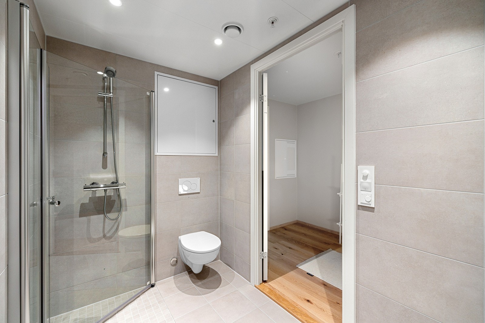 Badet er utstyrt med dusjhjørne i glass, vegghengt toalett og servant med underskap og speil. Galleribilde