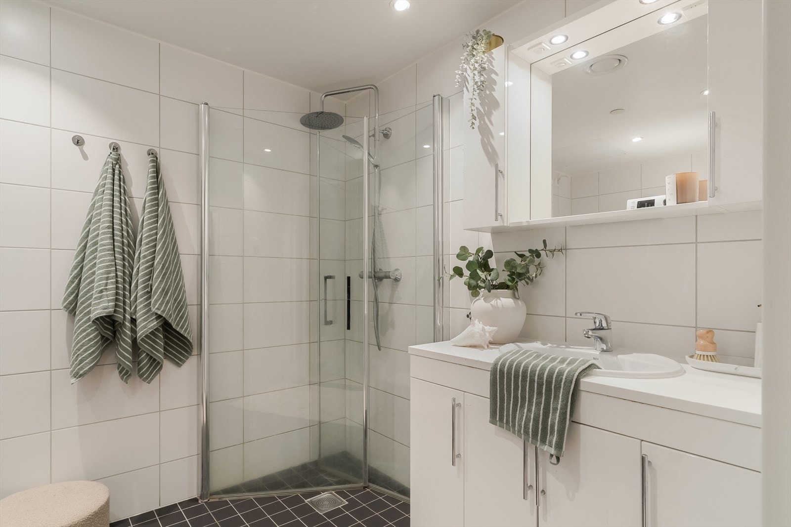 Badet er delikat og flislagt med dusjhjørne, vegghengt toalett og servant med oppbevaring. Galleribilde