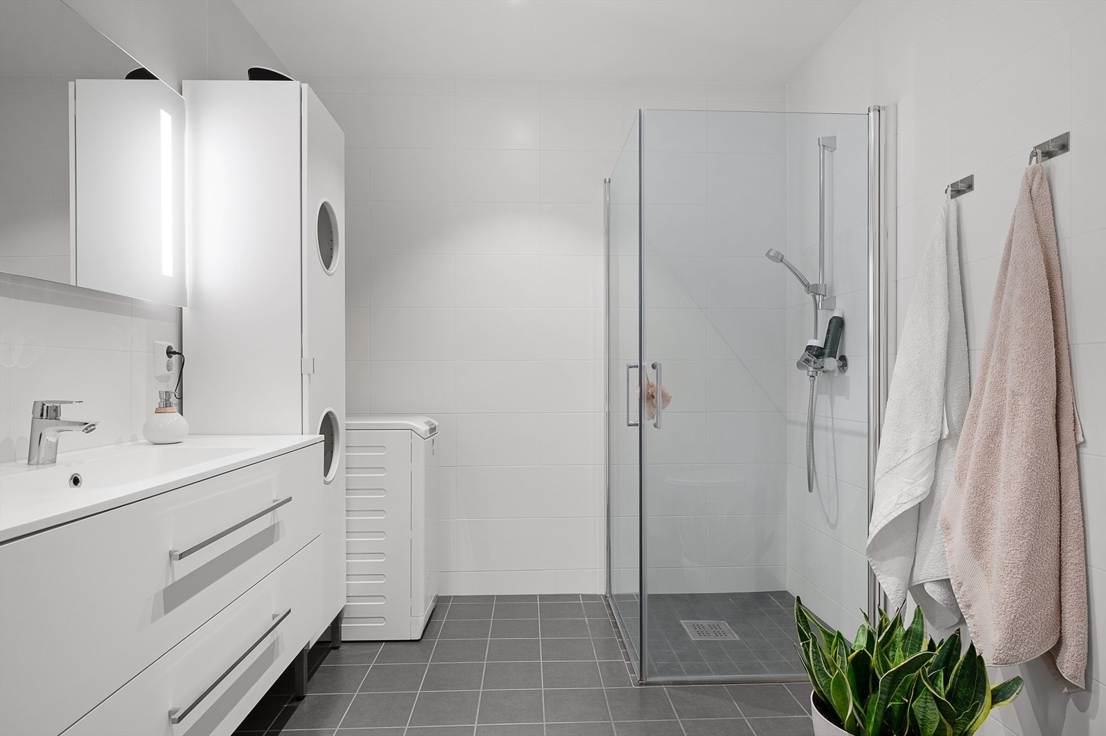 Lekkert bad som er flislagt med varmekabler i gulv. Hvit høyglans innredning, stort dusjhjørne med glassvegger mv. Opplegg til vaskemaskin. Galleribilde