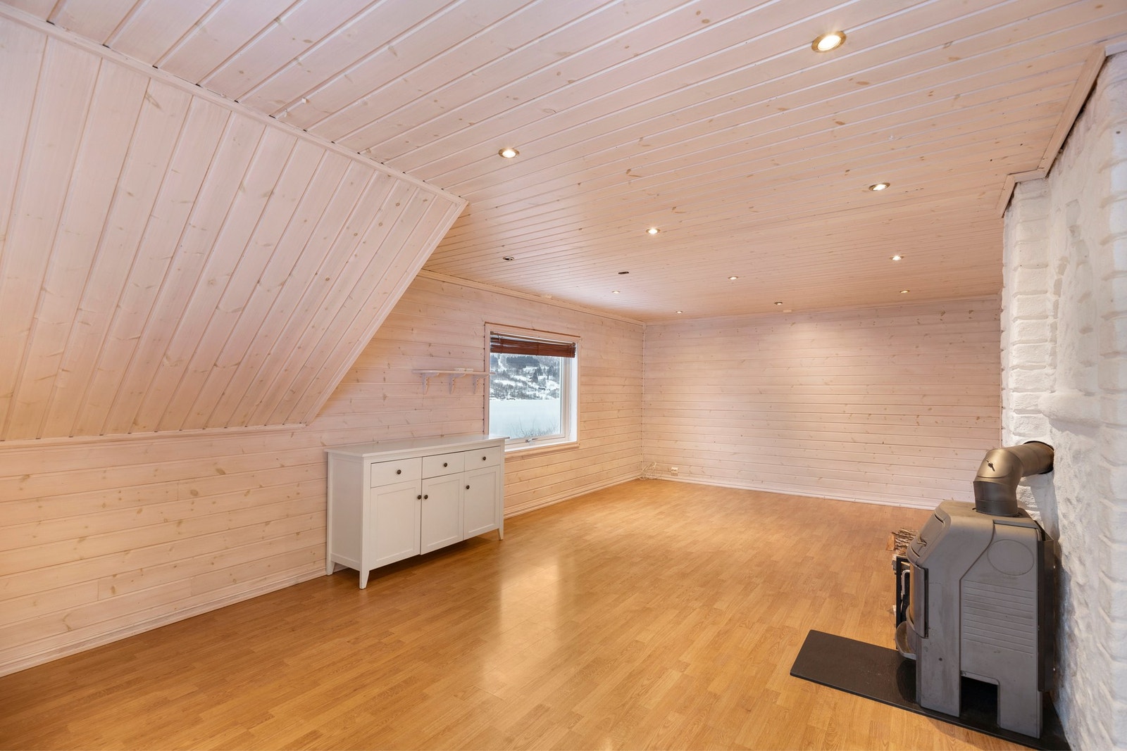 Her er det laminat på gulv, panel på vegger og spotlights i himling. Rommet har oppvarming fra vedovn. Galleribilde