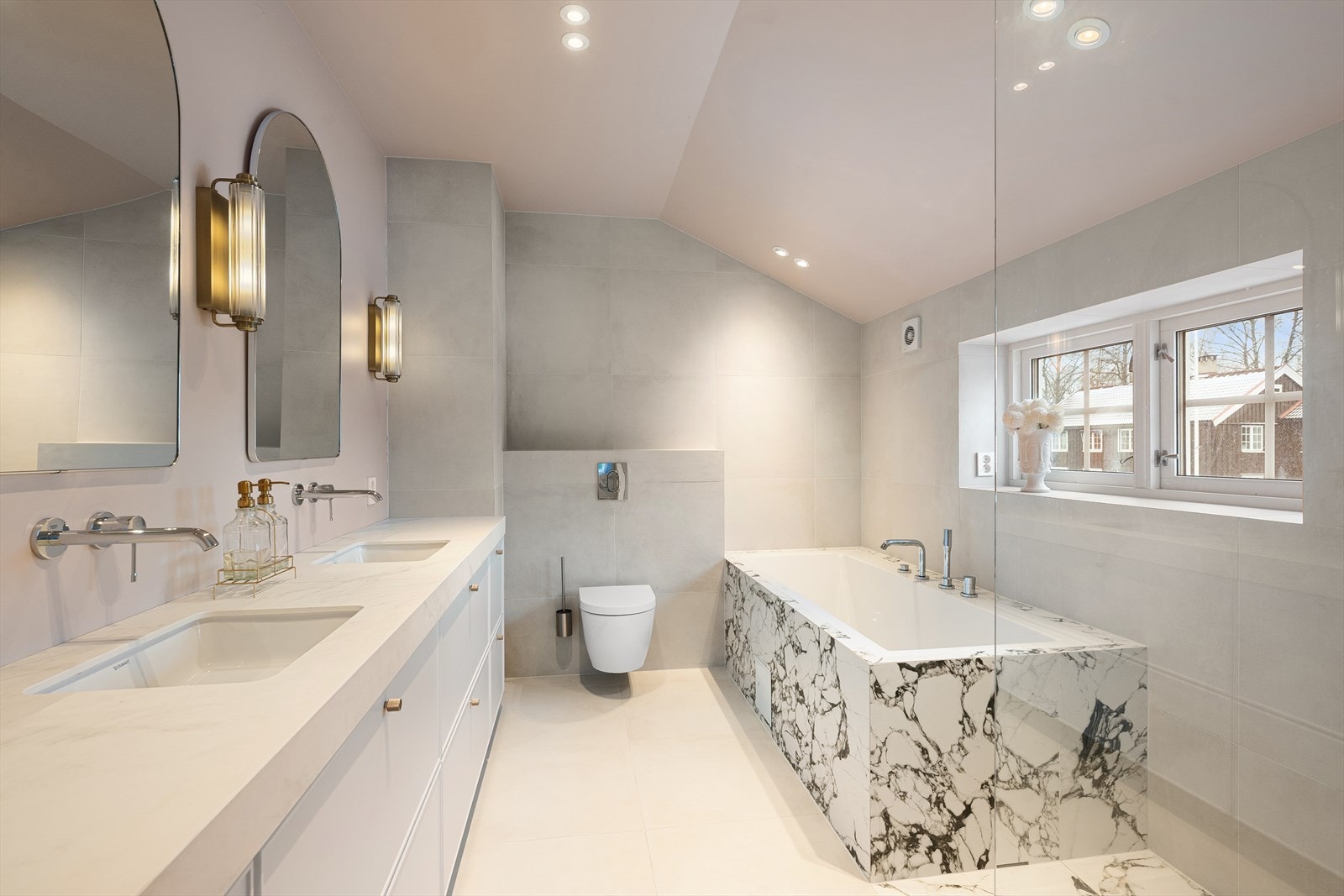 Innredningen består av skuffeløsning med heldekkende benkeplate i komposittstein og to underlimte servanter fra Duravit. Videre er det veggmontert toalett, innfliset badekar samt dusjhjørne med fastmontert dusjvegg og regnfallsdusj. Galleribilde