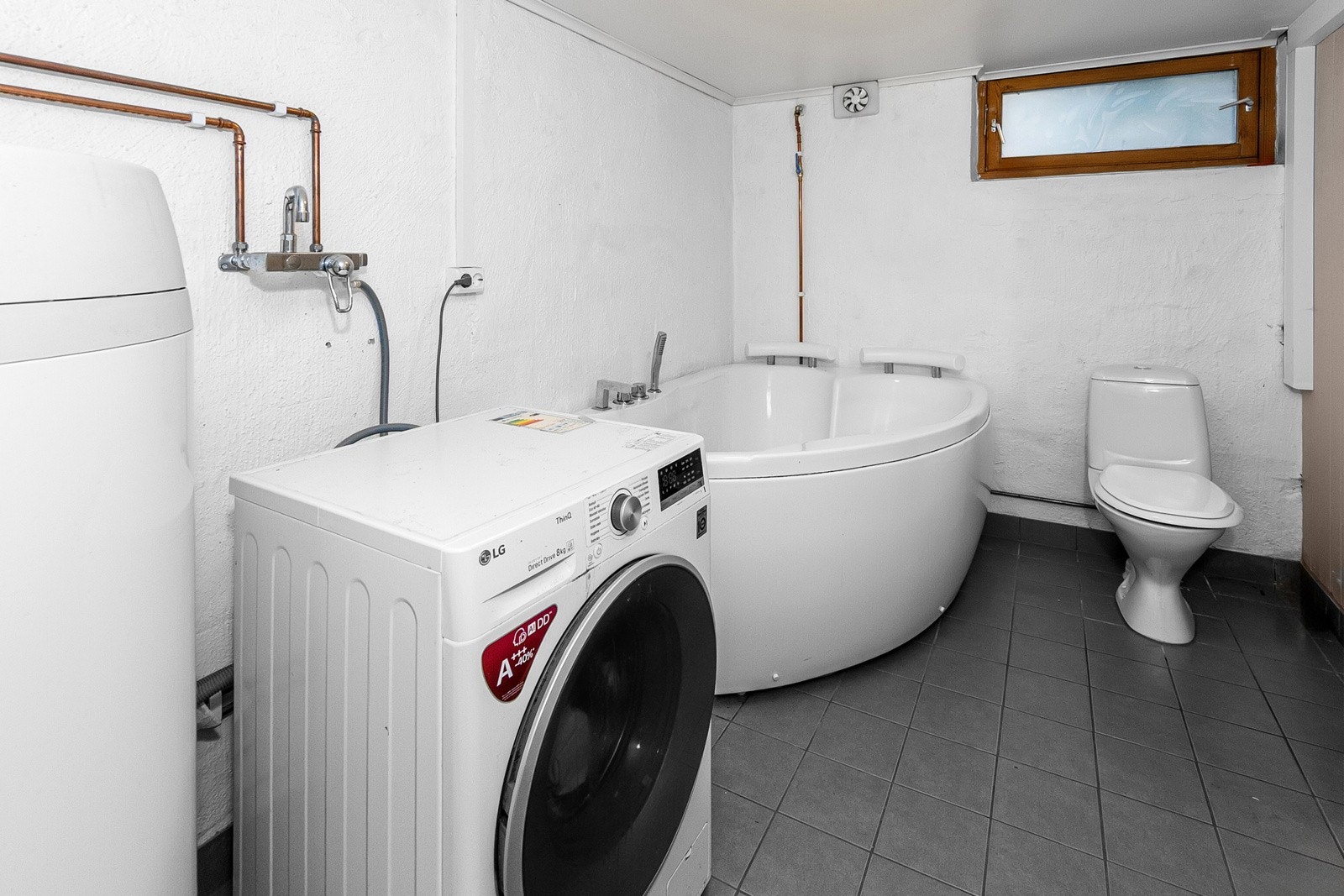 Vaskerom i kjeller med hjørnebadekar, gulvmontert toalett, VV bereder og opplegg til vaskemaskin. Galleribilde