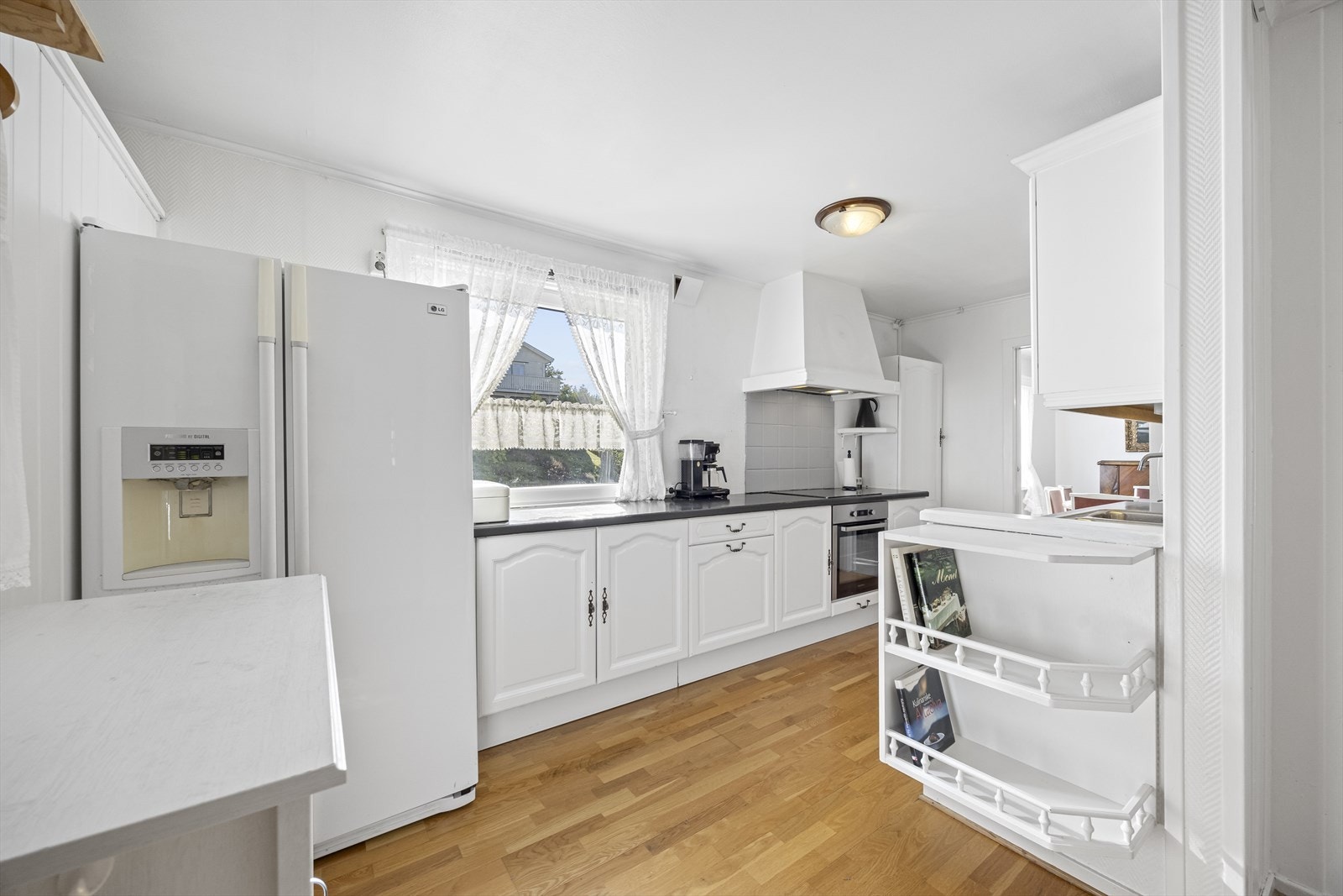 Kjøkkenet har innredning i hvit, profilert utførelse med integrert komfyr med koketopp, oppvaskmaskin og side-by-side frys- og kjøleskap hvor alt medfølger. Galleribilde