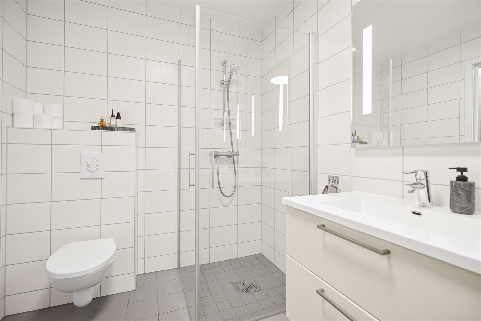 Bad/vaskerom inneholder vegghengt toalett, dusjhjørne og servant med to skuffer. Galleribilde