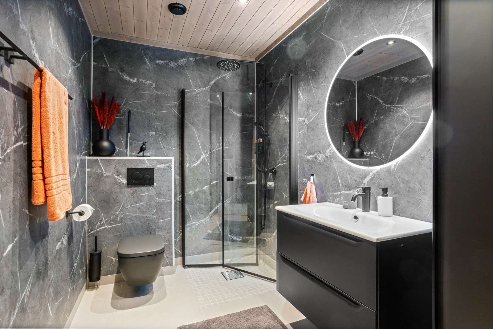 Badet i leiligheten er påkostet og fremstår som både funksjonelt og stilrent, med moderne uttrykk og gjennomgående helhet i material- og fargevalg. Dusjhjørnet er utstyrt med innfellbare dusjdører i sort profil med dusjarmatur i dempet sort. Galleribilde