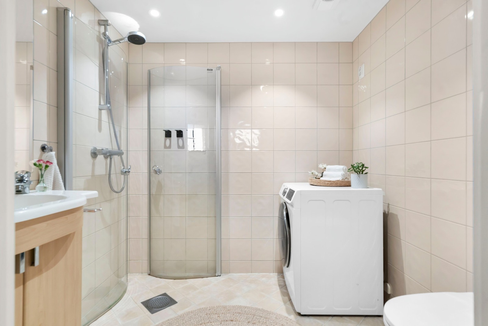 Flislagt bad med vegghengt toalett, servantinnredning med vask og skap, dusj rett på flis, samt opplegg for vaskemaskin og tørketrommel Galleribilde