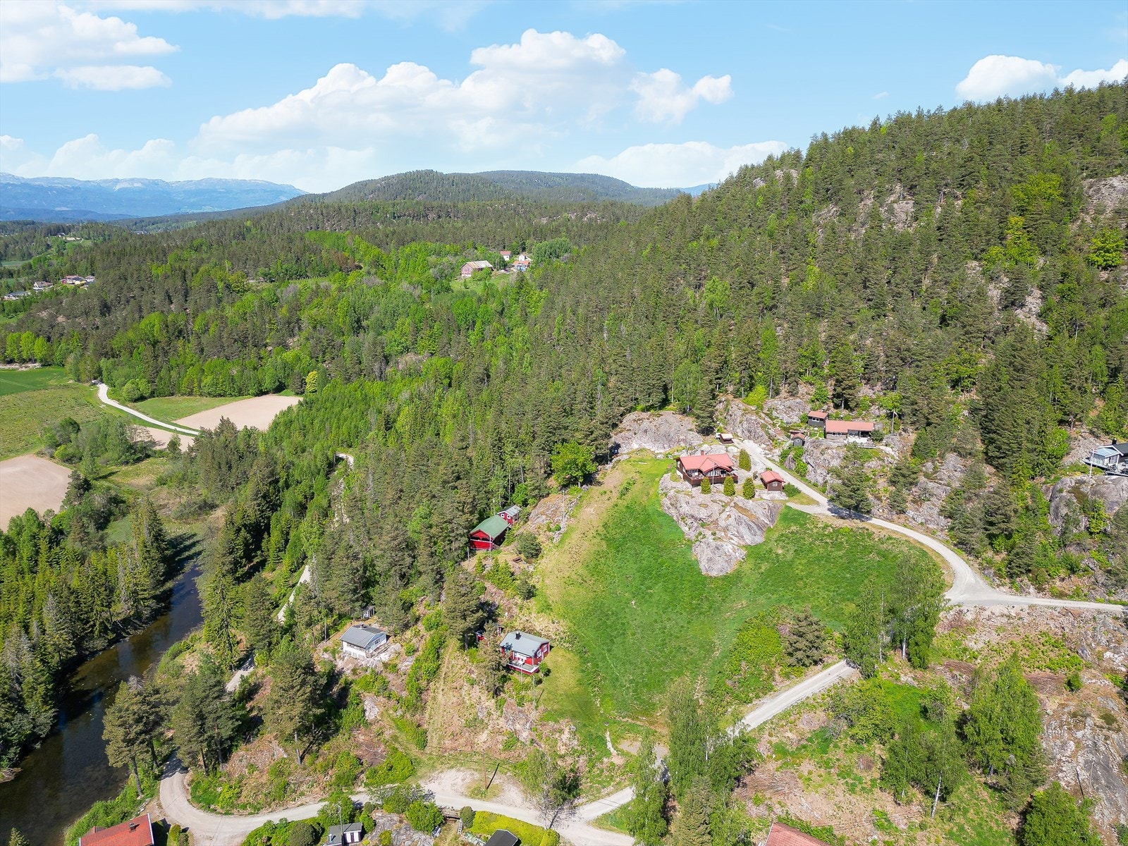 Tomten er en naturtomt med gress, trær og fjell i dagen. Galleribilde