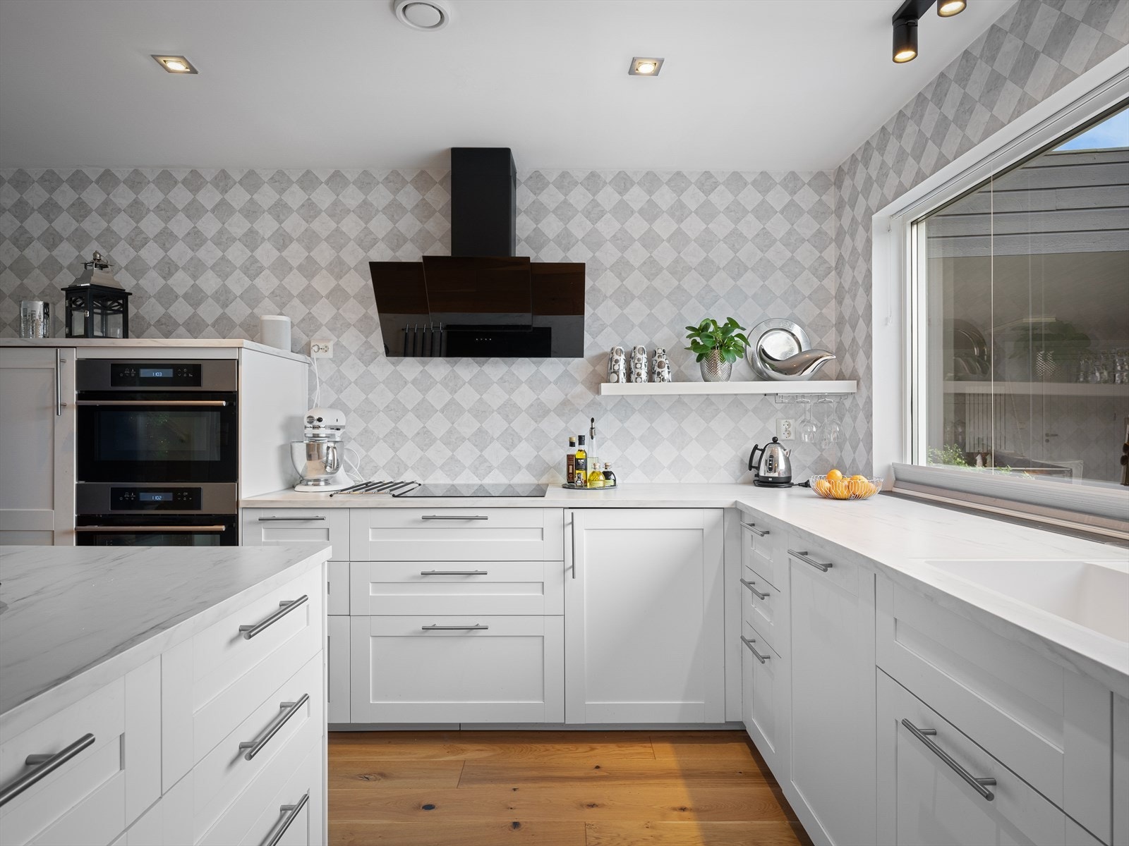 Pene kontraster mellom 1-stavs kvalitetsgulv og hvite, moderne kjøkkenfronter. Rikelig med naturlig lys fra flere vinduer. Hvitevarer i arbeidshøyde og luftig løsning uten overskap. Galleribilde