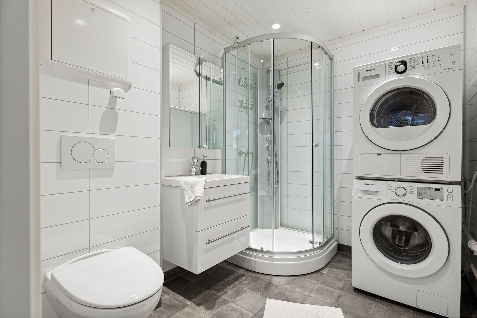 Lekkert bad med vegghengt toalett, dusjhjørne, vaskemaskin, tørketrommel og varme i gulv. Galleribilde
