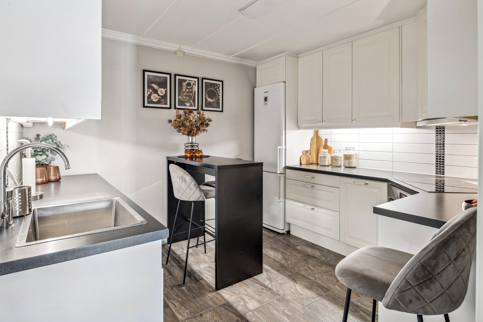 Lys og pen kjøkkeninnredning med god skap- og benkeplass. Innredningen har lyse profilerte fronter, laminert benkeplate med nedfelt oppvaskkum, fliser i benkeryggen og belysning under overskapene. Galleribilde