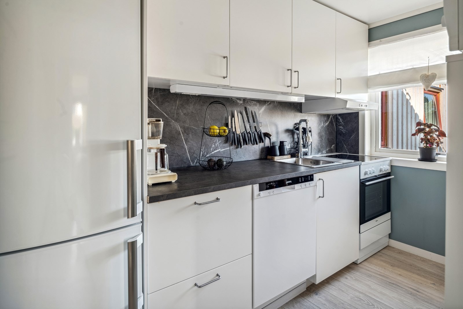 Moderne kjøkkeninnredning fra 2021/22 med hvite glatte fronter og laminert benkeplate med nedfelt oppvaskkum. Praktisk med plater i benkeryggen og takhøye overskap med belysning under. Galleribilde