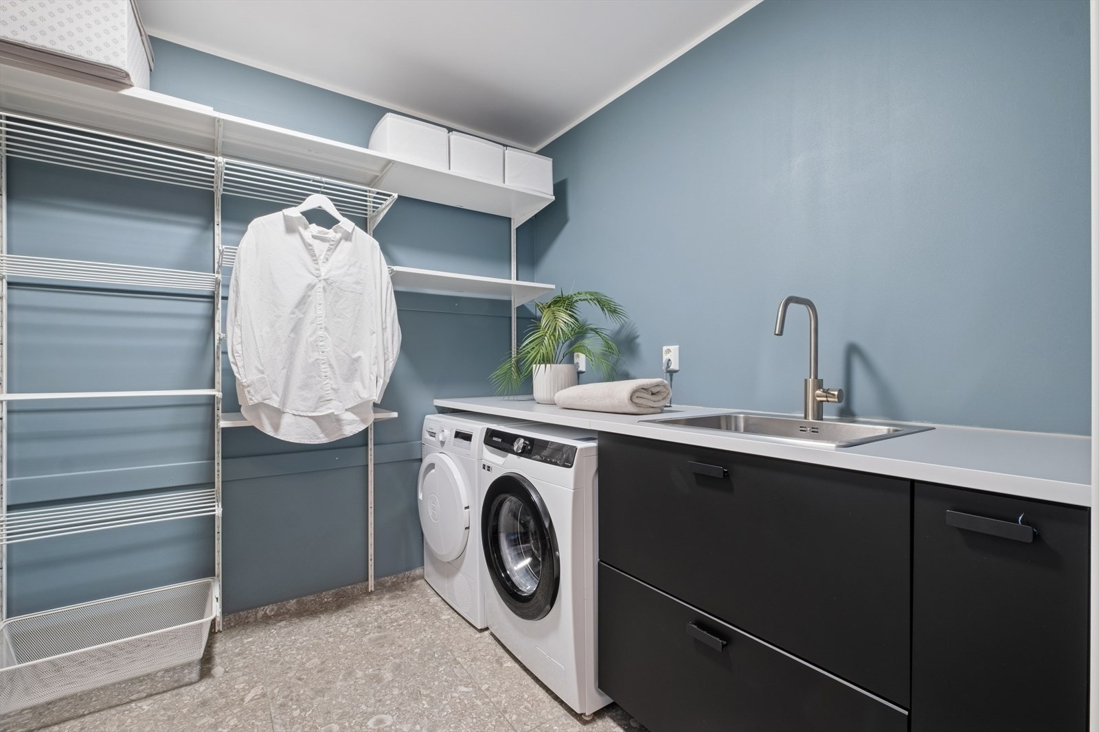 Vaskerommet har flislagt gulv som har termostatstyrt vannbåren gulvvarme. Rommet har innredning med slette fronter, laminat benkeplate med vask, hyllesystem, samt opplegg for vaskemaskin og tørketrommel. Galleribilde