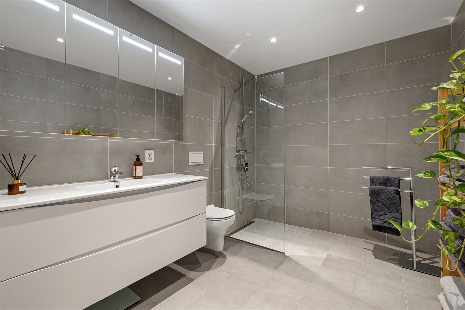 Stort og moderne bad med fliser, varmekabler, nedfelt servant, romslig underskap, veggfestet toalett og praktisk dusjhjørne. Galleribilde