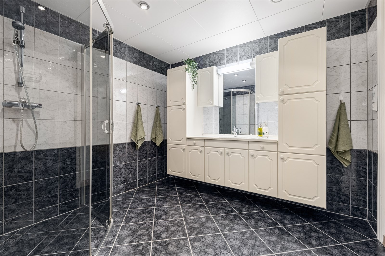 Badet er innredet med servantinnredning, speil, gulvmontert toalett og dusj med glassdører. Galleribilde