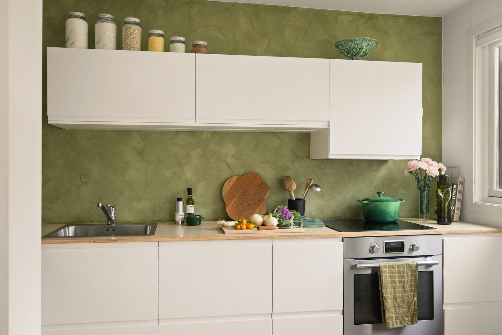 Mellom benkeplate og overskap er det slette, malte vegger i en delikat grønnfarge som tilfører rommet et særpreg og en behagelig kontrast til de lyse flatene. Galleribilde