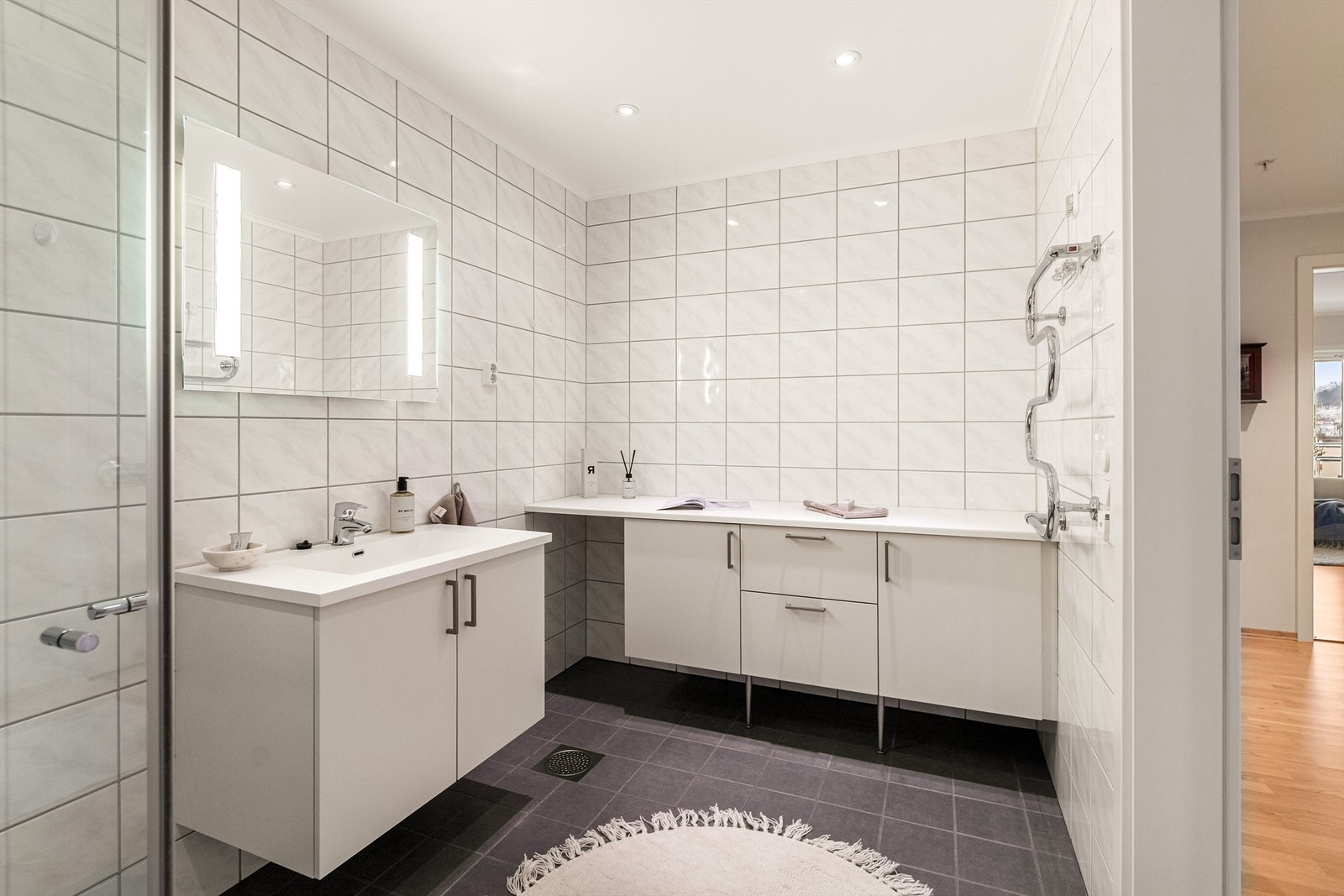 Badet er godt innredet med håndkleholder, servant i innredning, dusjhjørne og toalett. Ekstra skaper med benkeplate for oppbevaring av håndkler etc Galleribilde