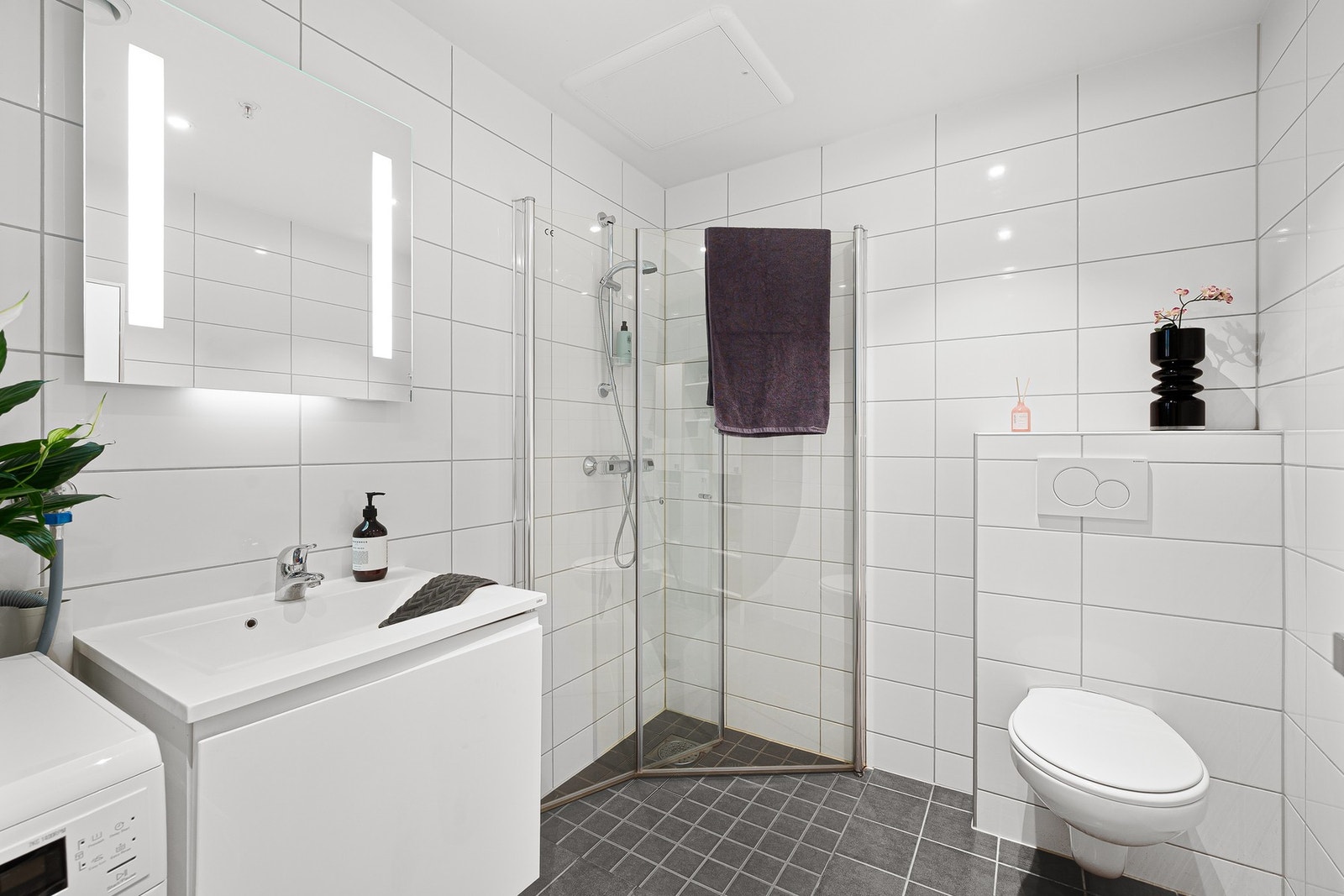 Pent bad med dusjhjørne, vegghengt toalett og servant på underskap. Galleribilde