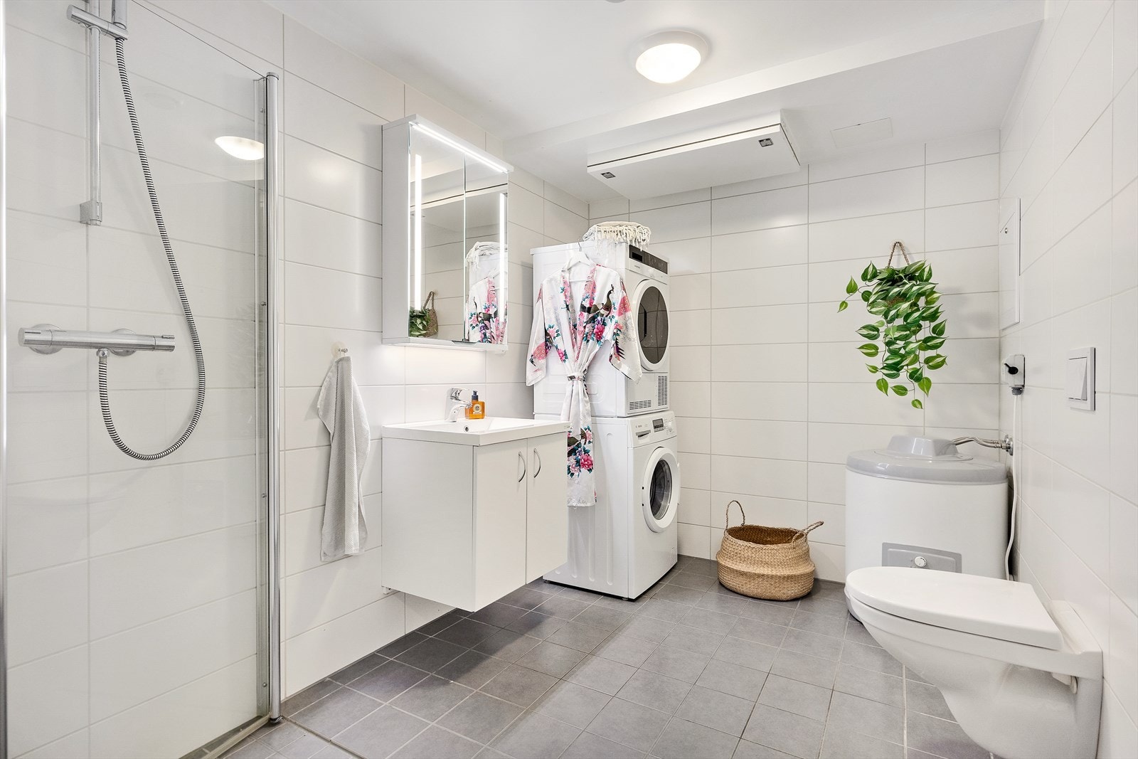 Flislagt bad med varme i gulv. Badet inneholder vegghengt toalett, servant med skapseksjon, speilskap med belysning, varmtvannsbereder og opplegg for vaskemaskin/tørketrommel. Galleribilde