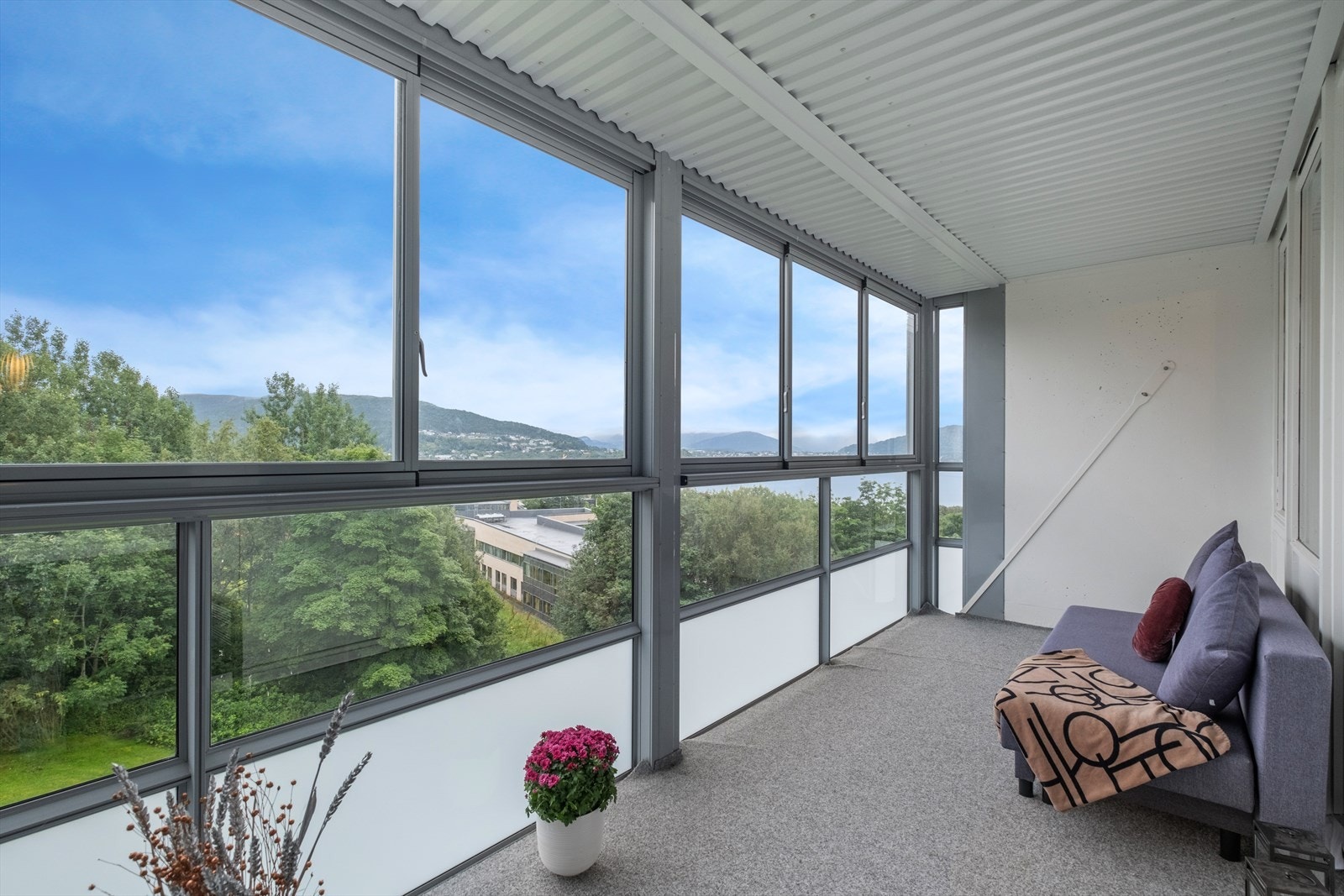 Balkongen har et dekke av betong med teppe, og store vindusflater gir lys og utsikt. Galleribilde