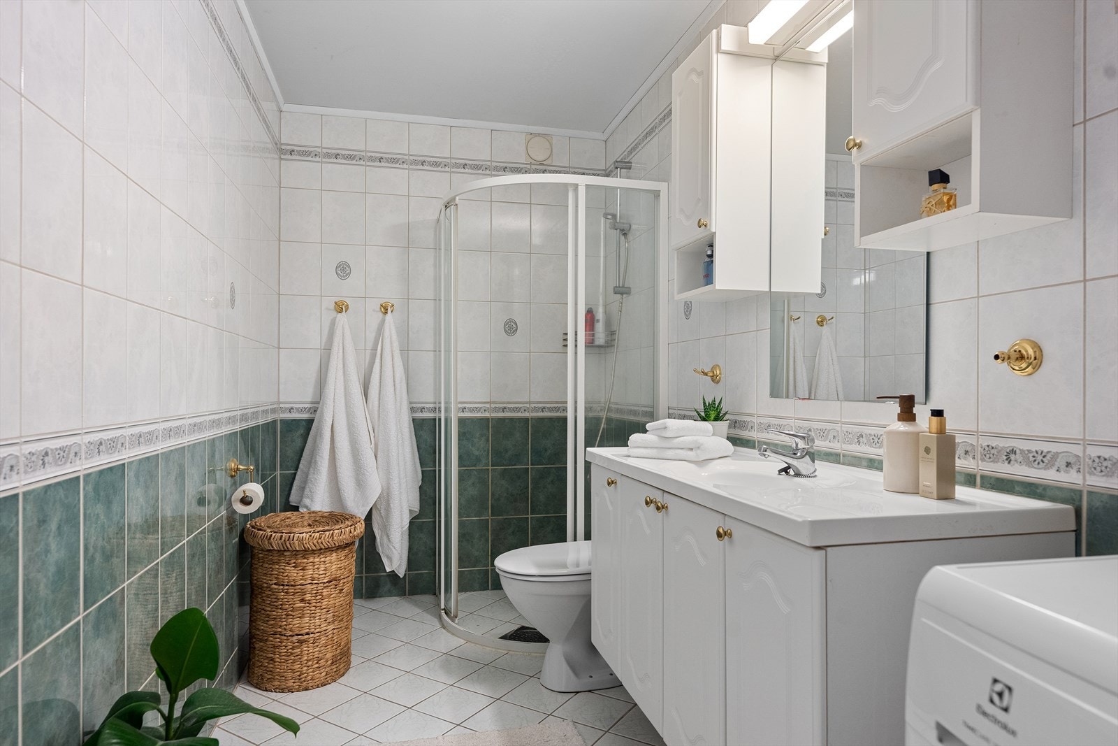 Romslig flislagt baderom, med baderomsinnredning bestående av benkeskap og veggskap med profilerte fronter, samt toalett og dusjhjørne. Galleribilde