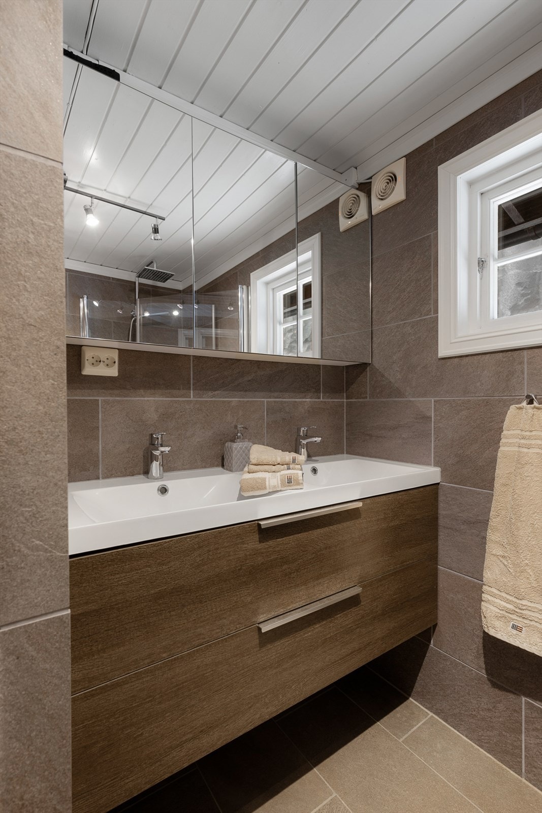 Badet er innredet med baderomsmøbel med servant, speilskap, dusjvegger og vegghengt toalett. Galleribilde