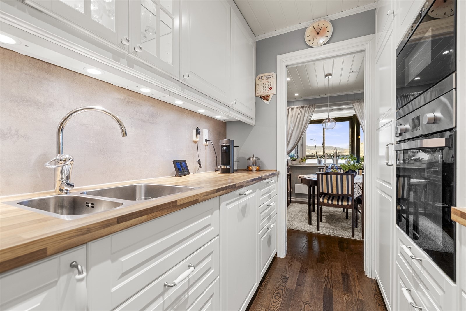 Her er det profilerte fronter, benkeplate i laminat, kjøkkenplater på vegg over benkeplate og belysning under overskap. Det er også integrerte hvitevarer som platetopp, stekeovn, mikrobølgeovn, oppvaskmaskin og kjøle-/fryseskap. Galleribilde