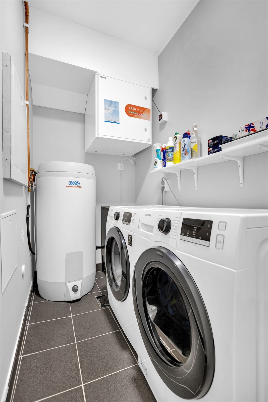 Teknisk rom med flislagt gulv, malte vegger og himling. Her er det opplegg for vaskemaskin, samt bereder, stoppekran i luke, rørfordelerskap, sikringsskap og ventilasjonsaggregat. Galleribilde