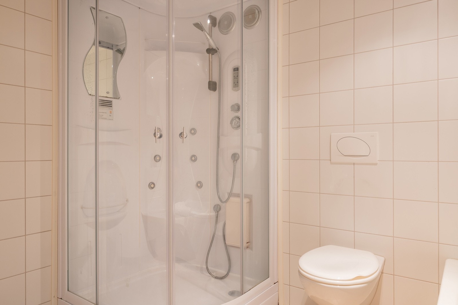 Badet har innredning med veggmontert toalett, dusjkabinett og badekar. Ventilasjon med elektrisk styrt avtrekksvifte Galleribilde