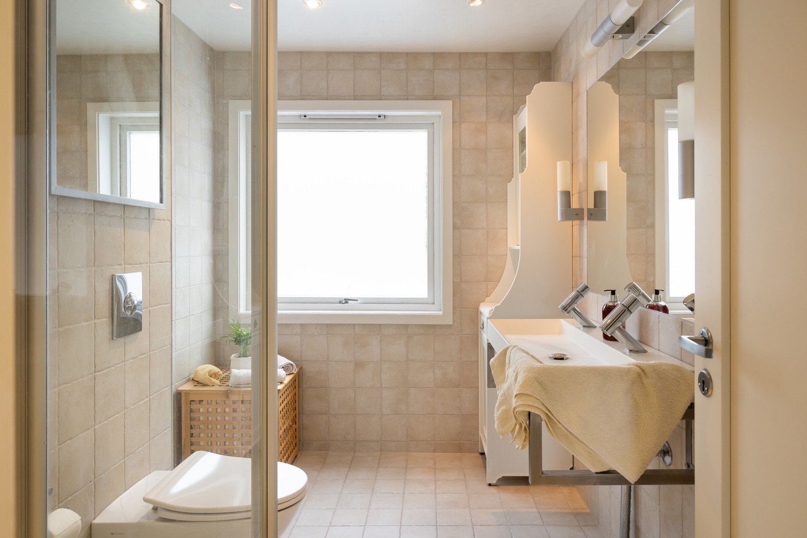 Lyst flislagt baderom med elektriske varmekabler, dusjhjørne og gode oppbevaringsløsninger Galleribilde