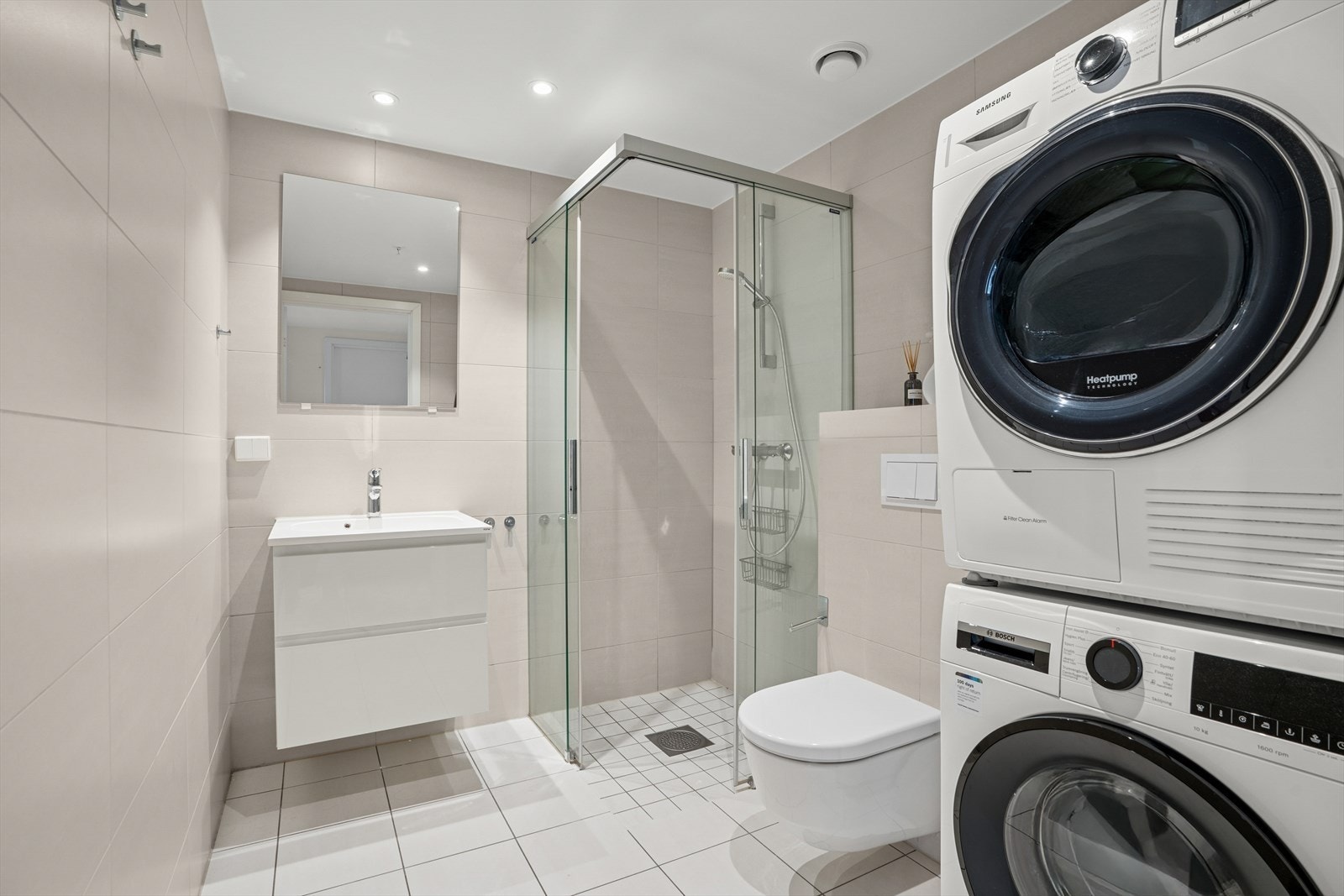 Badet er innredet med med servantskap med ett-greps blandebatteri, veggspeil, vegghengt toalett med innebygget sisterne, avskjermet dusjhjørne med glass, blandebatteri og dusjgarnityr. Galleribilde