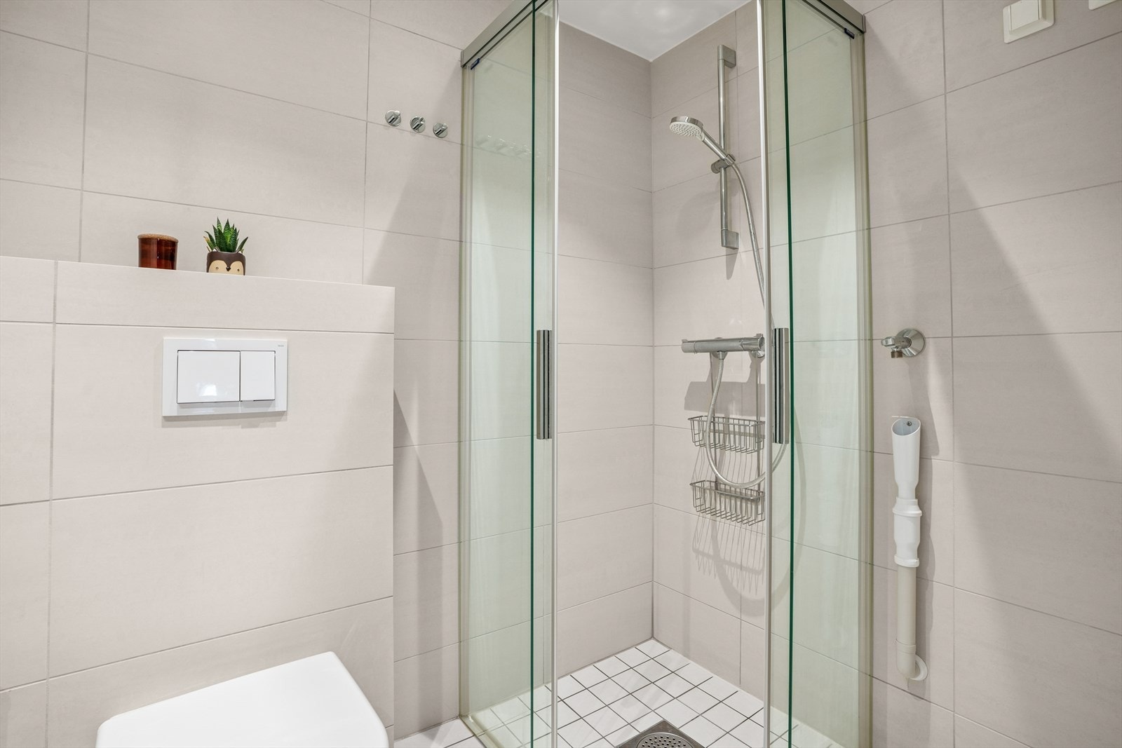 Badet er innredet med servantskap med ett-greps blandebatteri, veggspeil, vegghengt toalett med innebygget sisterne, avskjermet dusjhjørne med glass, blandebatteri og dusjgarnityr. Galleribilde