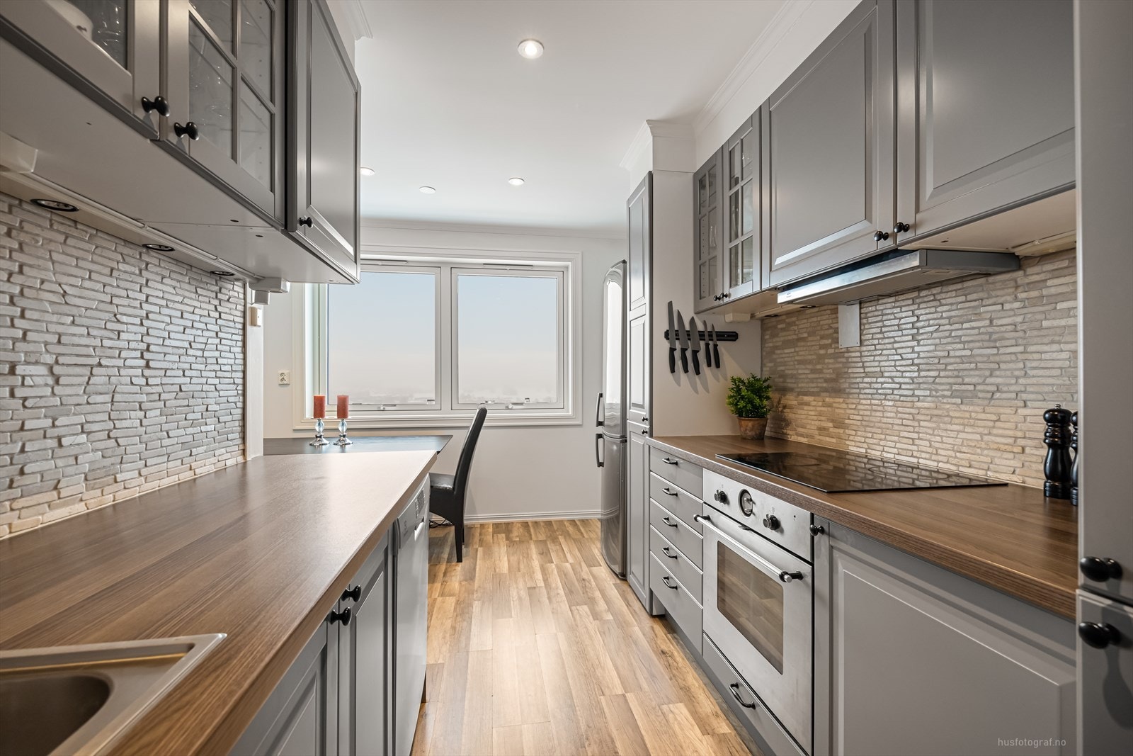 Pent kjøkken som er flissatt over benk, benkeplate er av laminat og det er profilerte grå fronter. Galleribilde