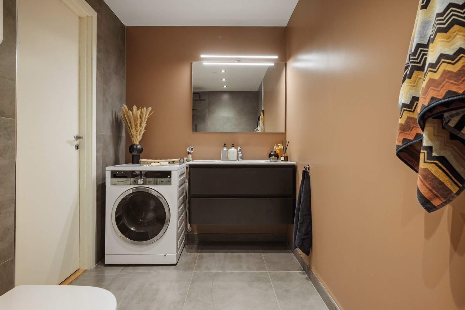 Badet er utstyrt med dusj, vegghengt toalett, opplegg for vaskemaskin og servant med innredning. Galleribilde