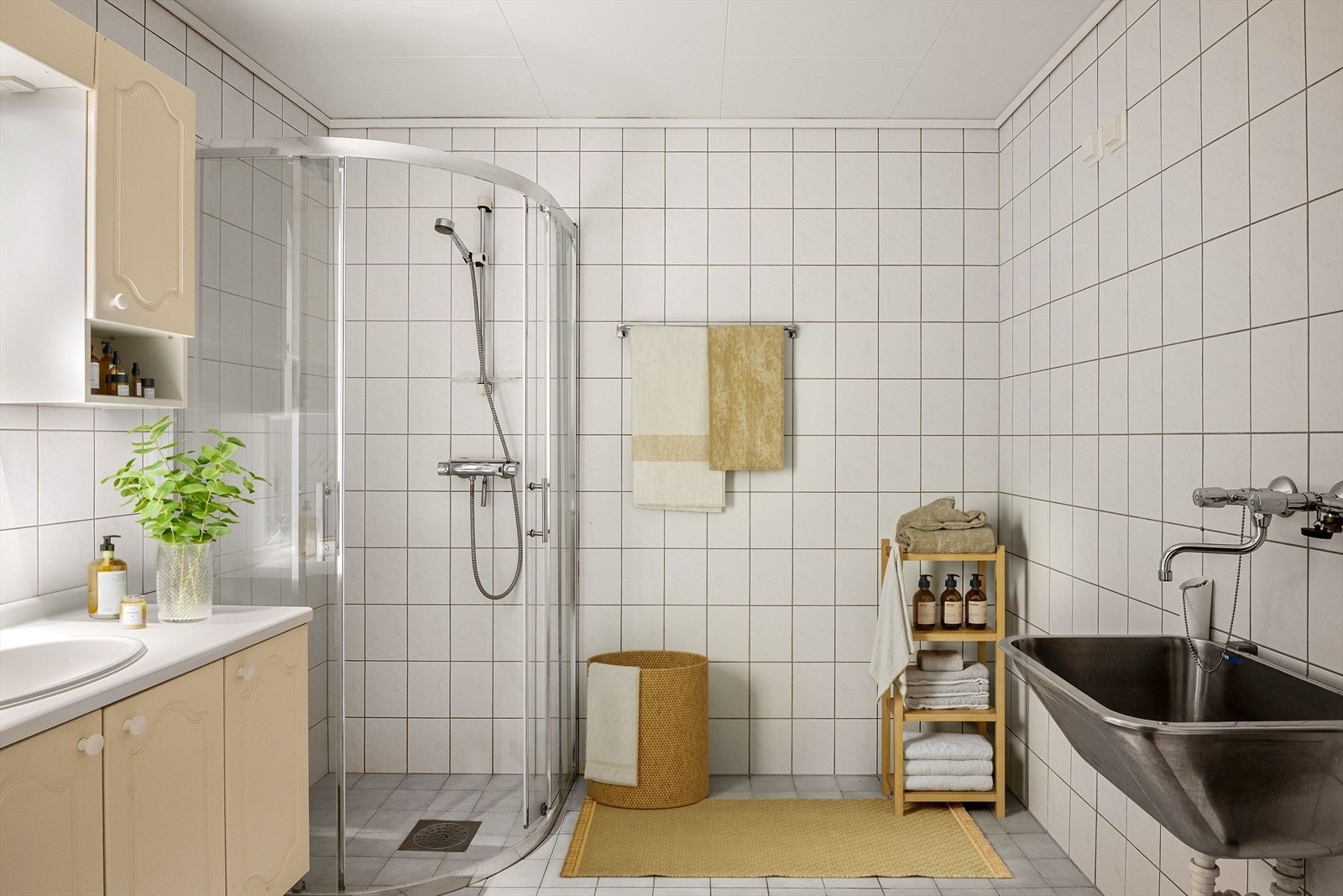 Flislagt baderom innredet med dusjkabinett, servant på innredning, speil med overskap samt utslagsvask. Galleribilde