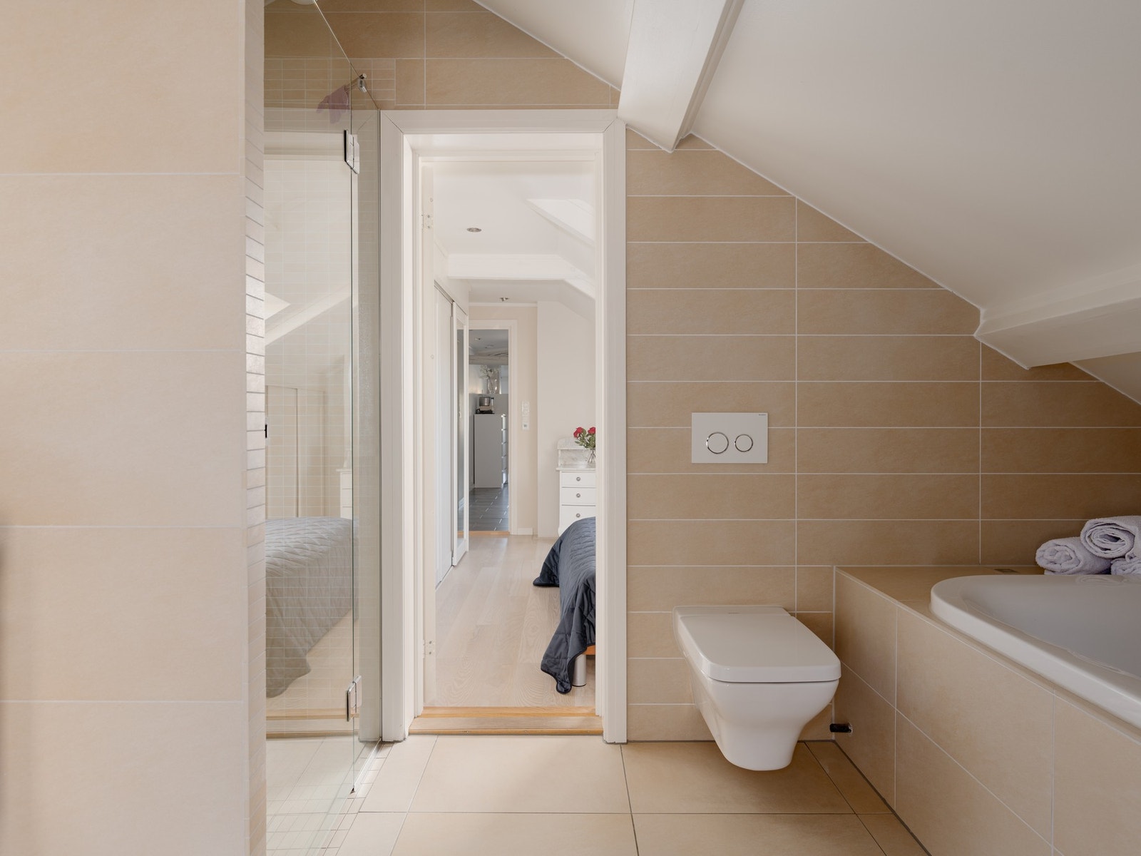 Det store baderommet inneholder innmurt badekar, dusj med glassdør, varmekabler i gulv, vegghengt toalett, belysning og vindu Galleribilde