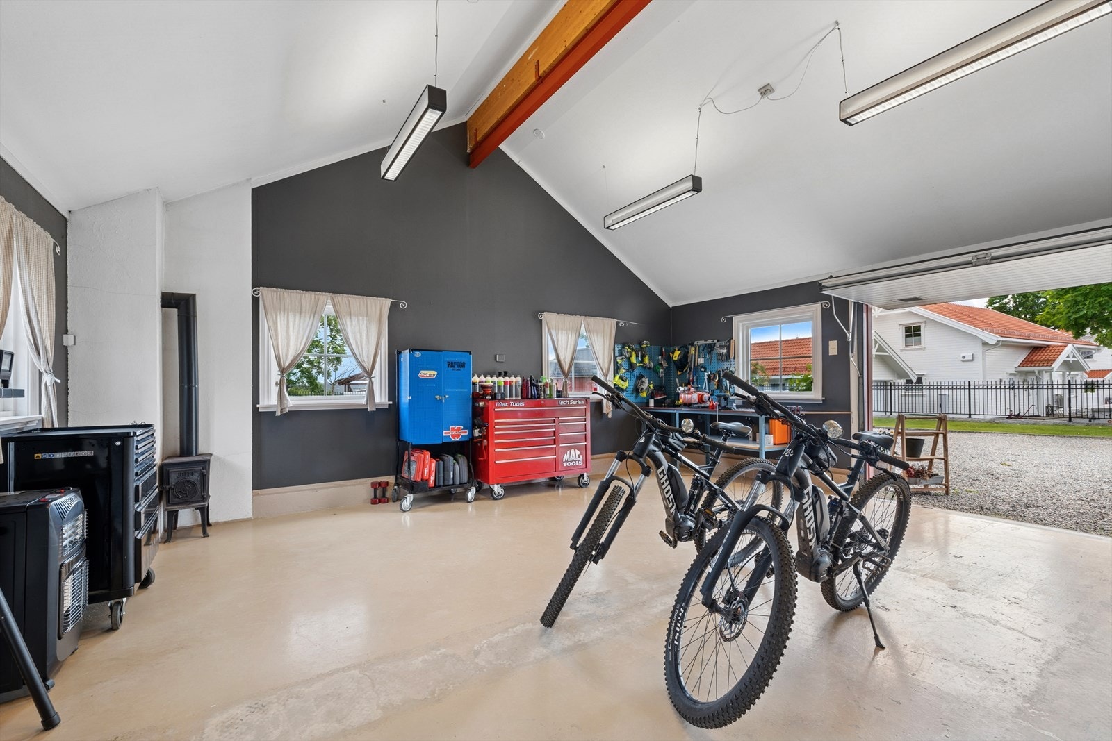 Garasjerommet/flerbruksrommet har lyse vinduer og en koselig vedovn, og egner seg godt til verksted, treningsrom eller lagring. Det er også en stor carport på baksiden av låven. Galleribilde