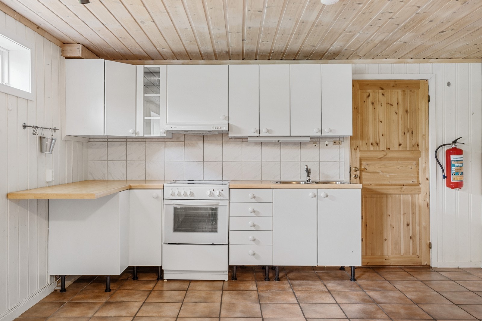 Kjøkkenet er enkelt innredet med slette fronter, laminat benkeplate og fliser på vegg over benk. Det er frittstående komfyr. Galleribilde