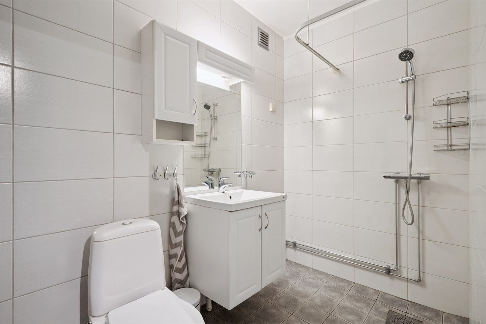 Badet er helfliset og innredet med dusjhjørne, toalett og servant med underskap. Galleribilde