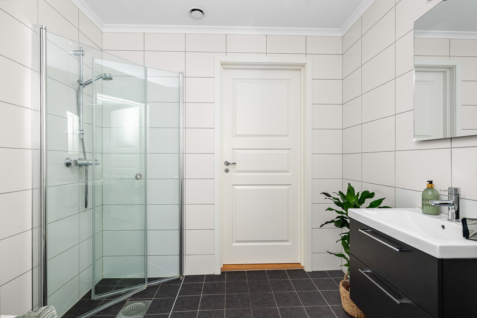 Pent bad med flis på gulv og vegger. Her er det vegghengt toalett, dusjhjørne med glassdører og garnityr, samt innredning med heldekkende hvit vask, underskuffer med slette fronter og speil.
Det er varmekabler i gulv og balansert ventilasjon. Galleribilde