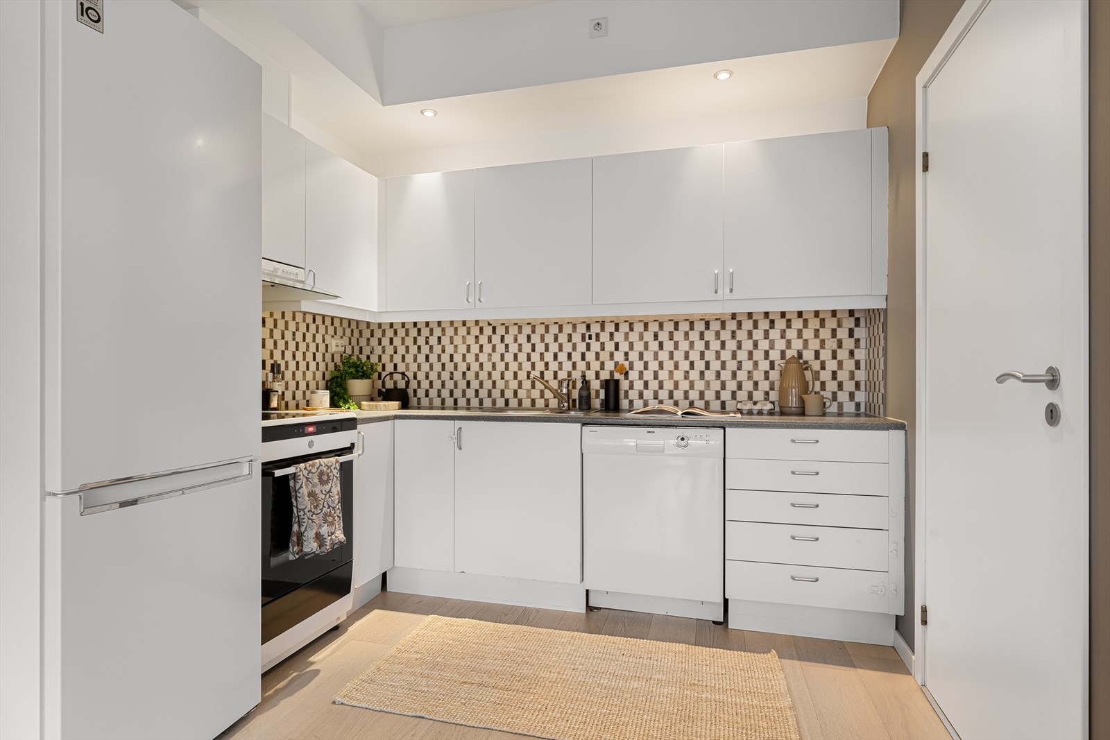 Kjøkkenet har hvite glatte fronter og laminert benkeplate med nedfelt kum i rustfritt stål Galleribilde