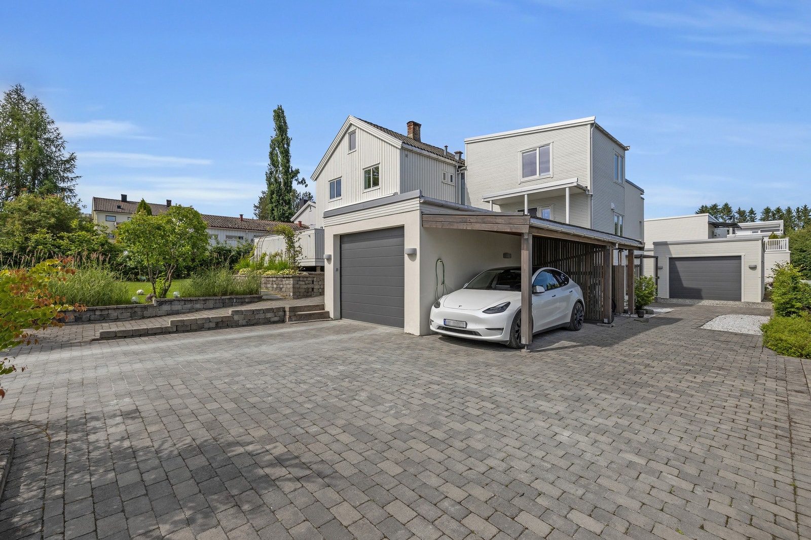 Steinlagt gårdsplass med gode parkeringsmuligheter i form av carport, to garasjer, egen leietakerparkering og montert elbillader. Galleribilde