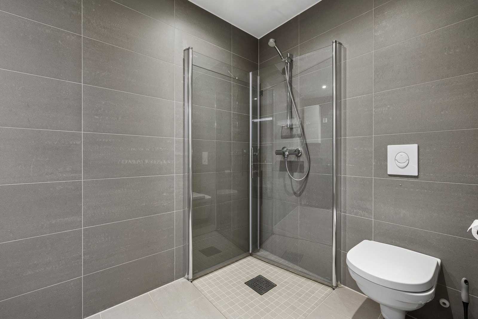 Badet er utstyrt med vegghengt toalett, dusjhjørne med svingbare glassvegger, samt baderomsinnredning med nedfelt servant og speil, samt opplegg for vaskemaskin. Galleribilde