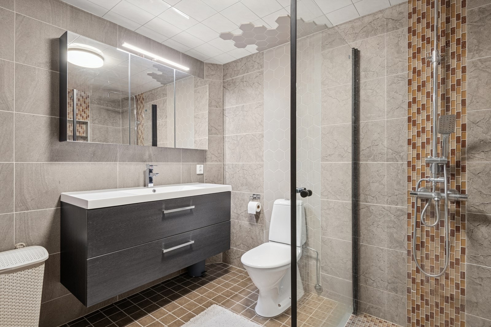 Helfliset baderom med dusjhjørne med glassvegg og vegghengt toalett. Galleribilde