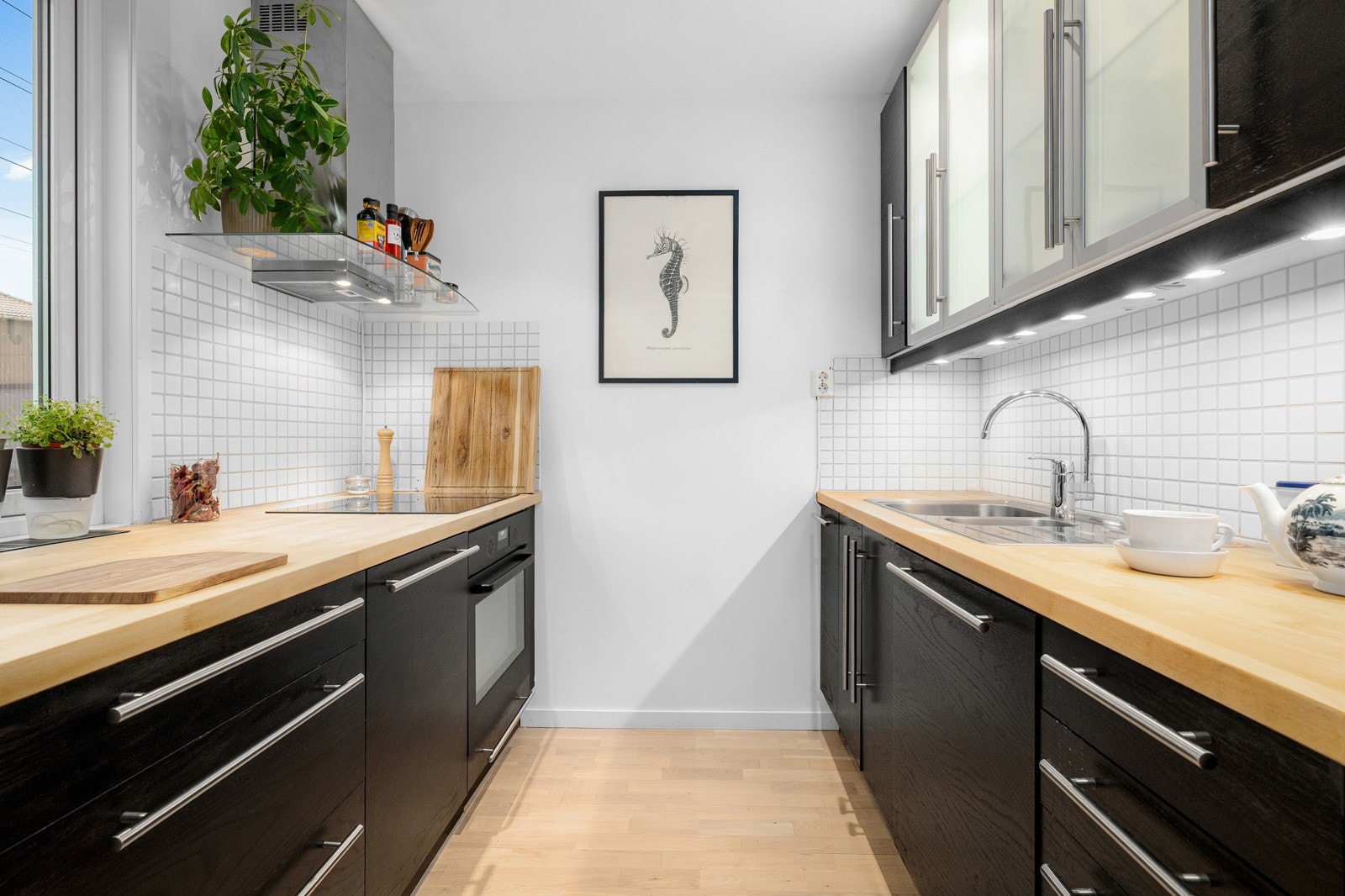 Moderne kjøkkeninnredning med sorte glatte fronter og benkeplate av tre med nedfelt oppvaskkum. Galleribilde