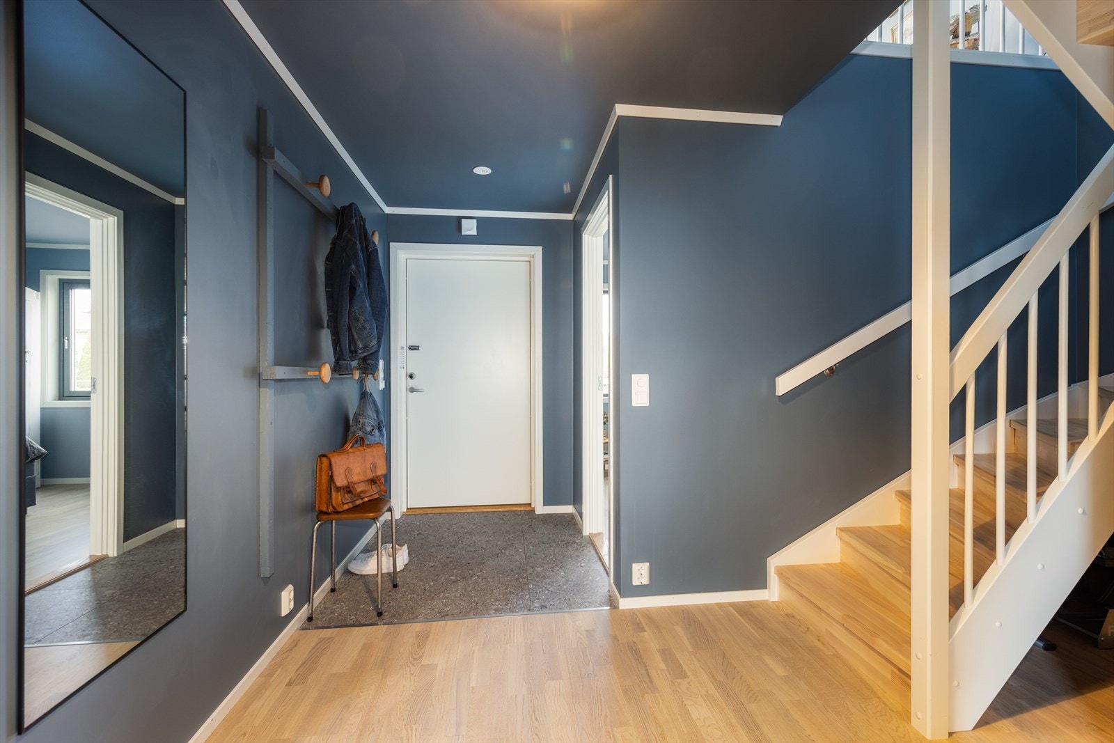Velkommen inn! Entreen har flislagt gulv med gulvvarme og praktisk oppheng for yttertøy. Herfra er det direkte adkomst til ett av soverommene i 1. etasje. Videre inn i hallen møtes du av et delikat uttrykk med lyst gulv og mørkeblå vegger. Galleribilde