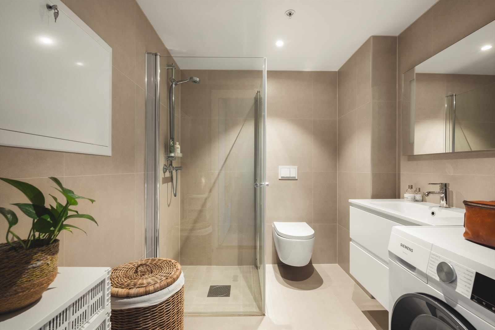 Lekkert og romslig bad utført med fliser på gulv - og veggflater, innredet med servant med underskap, toalett, dusjhjørne og opplegg for vaskemaskin. Galleribilde