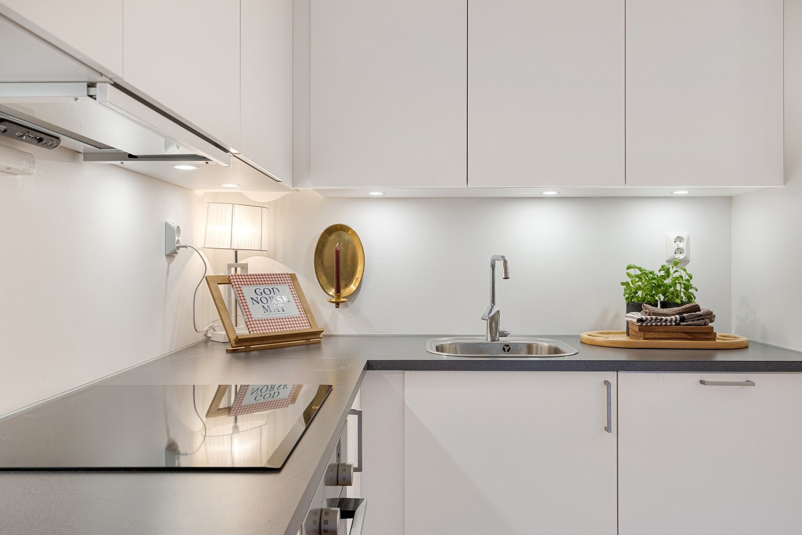 Kjøkkeninnredning med hvite glatte fronter, laminat benkeplate og benkebelysning under overskap. Galleribilde