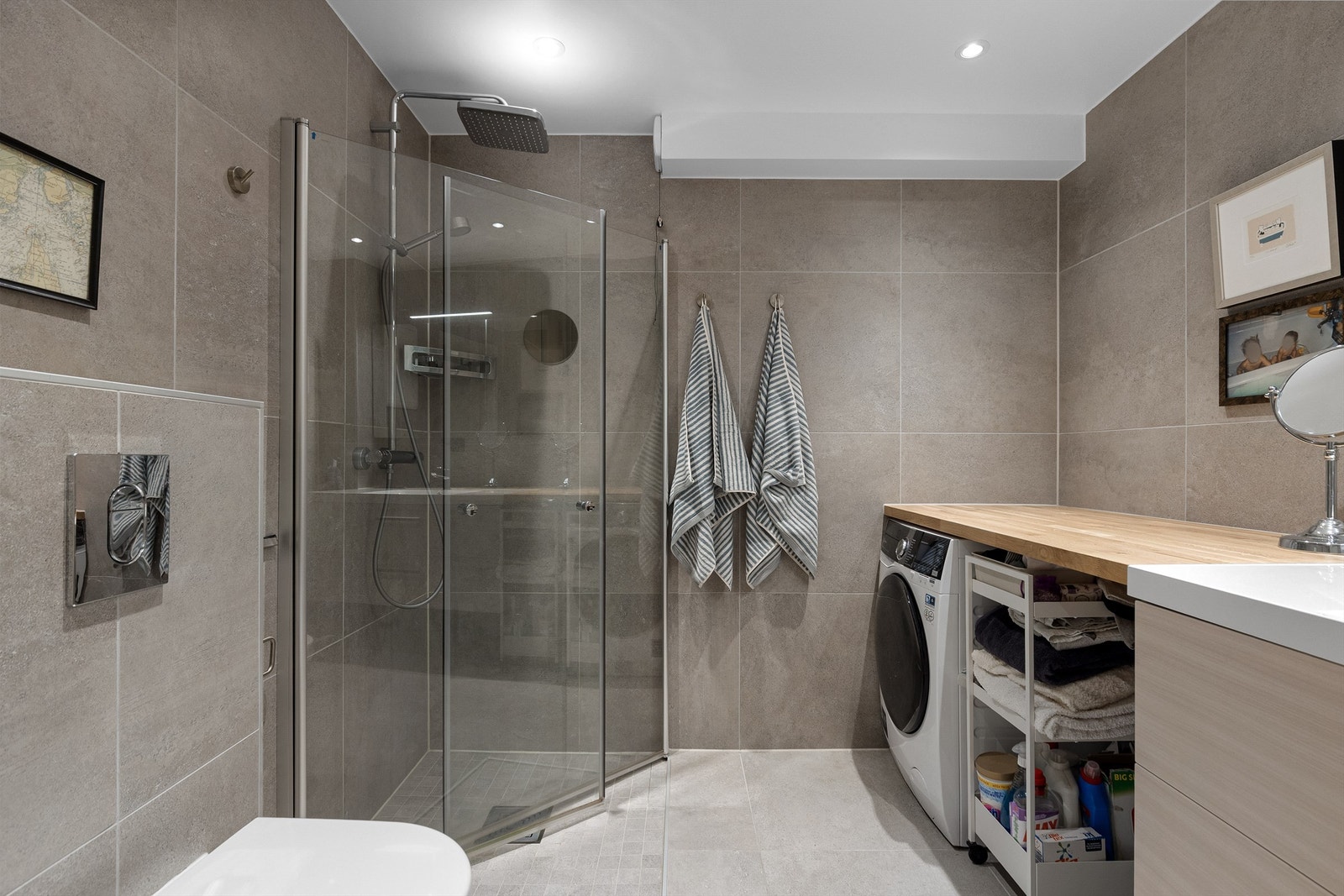 Badet har store fliser med betonglook, dusjhjørne med praktiske svingbare dører og armatur med regnsfallsdusj Galleribilde